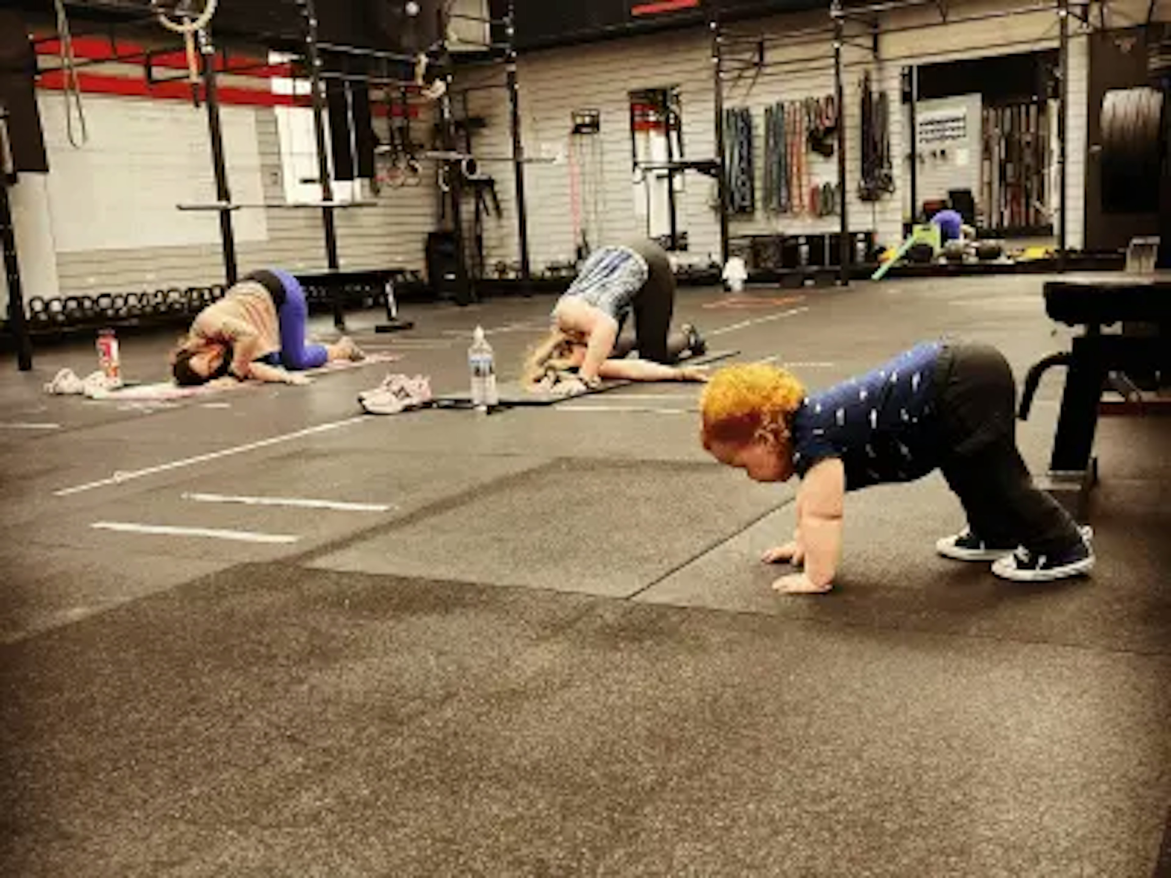 A baby practicing a gym exercise with other members of the gym.