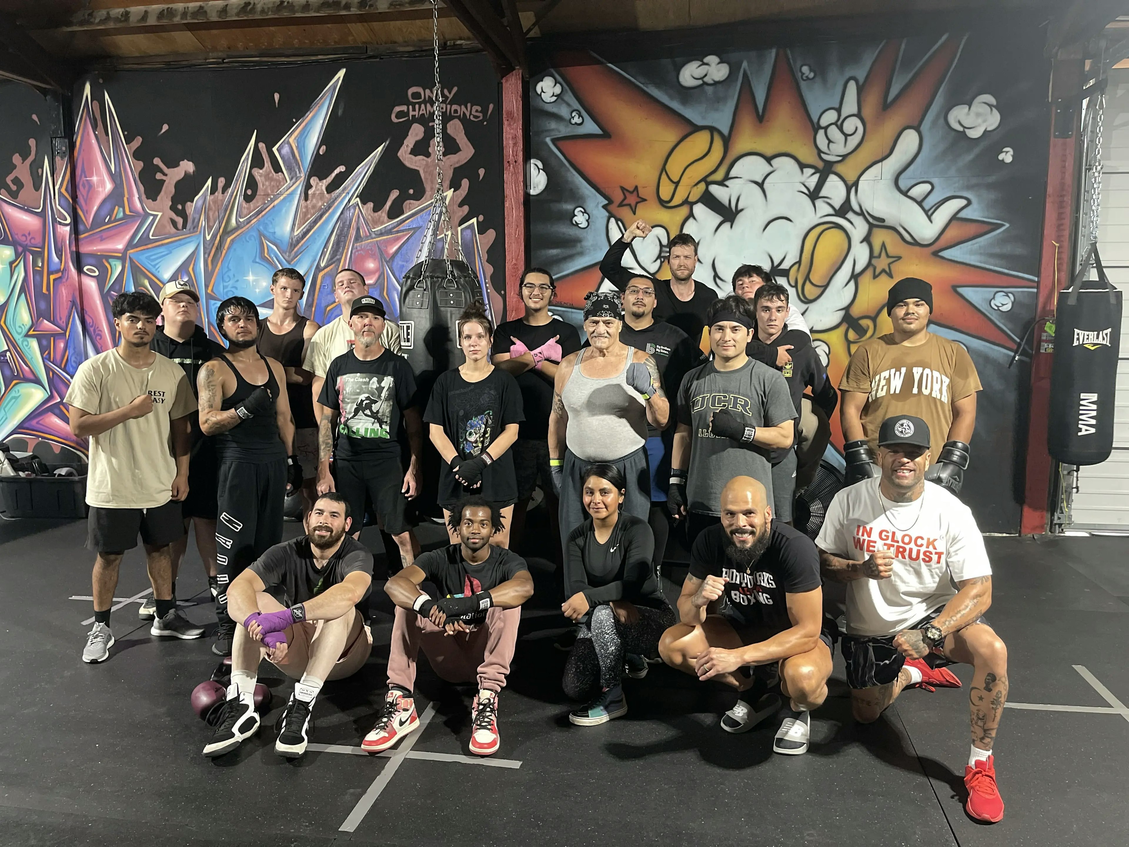 Group of boxing enthusiasts posing together after a training session in a gym with vibrant graffiti art in the background.